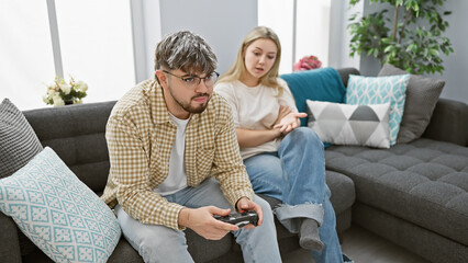A woman discusses with a man focused on playing videogames in a modern living room