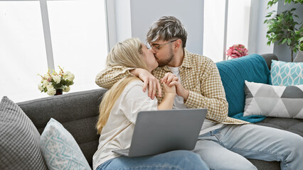 A loving couple kissing on a cozy sofa with a laptop in a modern living room