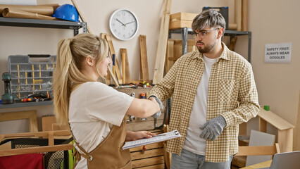 Man and woman in casual work attire shaking hands in a well-equipped carpentry workshop, indicating...