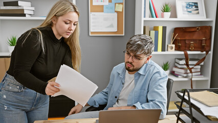 Focused man and woman review documents together at a modern office, showcasing teamwork and...