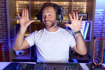 Middle age man with beard playing video games wearing headphones showing and pointing up with...