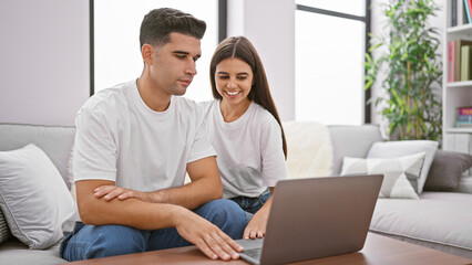 A smiling couple using a laptop together on a couch in a cozy living room.