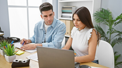 A man and woman coworking in a modern office with a laptop, discussing a project attentively.