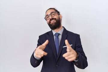 Hispanic man with beard wearing suit and tie pointing fingers to camera with happy and funny face....
