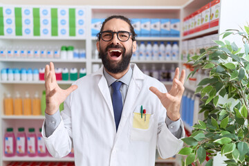 Hispanic man with beard working at pharmacy drugstore crazy and mad shouting and yelling with...
