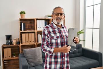 Senior grey-haired man business worker smiling confident holding clipboard at office
