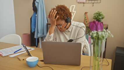 Stressed african american woman with headset working remotely in a home office.