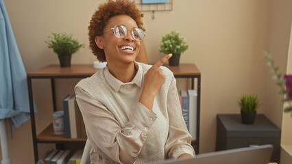 A cheerful african american woman wearing glasses indoors pointing while at a cozy home office...