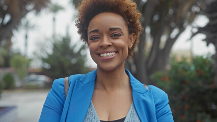 Smiling african american woman in a blue blazer posing outdoors with greenery in the background.
