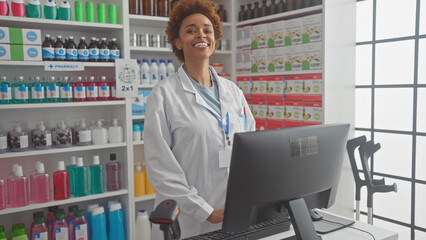 A smiling african american woman pharmacist standing in a pharmacy with shelves of medications in...