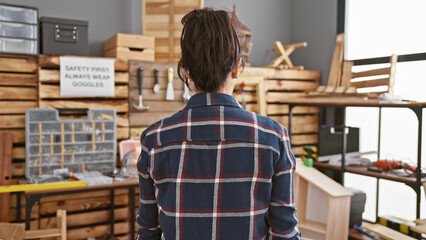 A woman in plaid attire standing pensively in a well-equipped carpentry workshop, representing...