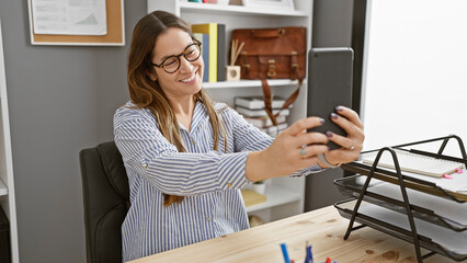 Smiling woman takes a selfie at her organized office desk, showcasing technology, professionalism,...