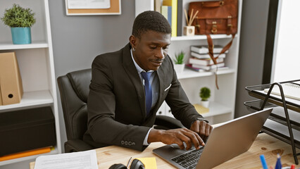 Handsome african american businessman working on a laptop in a modern office setting.