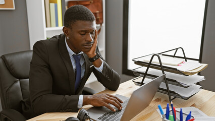 African american man stressed in a modern office using a laptop
