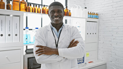 Confident african man in white lab coat standing with arms crossed in a bright laboratory