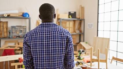 Back view of a thoughtful african man standing in a busy carpentry workshop.