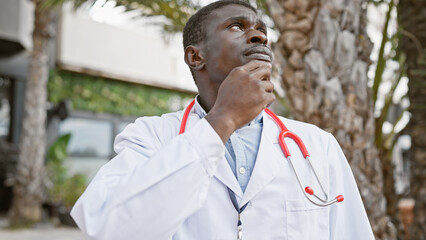 A thoughtful african american male doctor with a stethoscope standing outdoors in an urban setting.