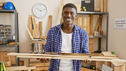 Handsome man with wood at a carpentry workshop, wearing casual clothes in a professional setting.