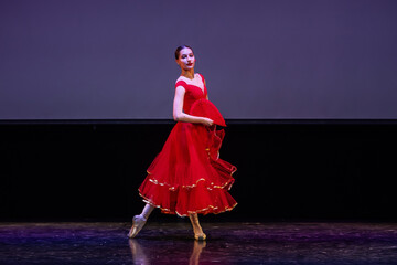 ballerina in a red dress performs a variation from the ballet Don Quixote on the theater stage.