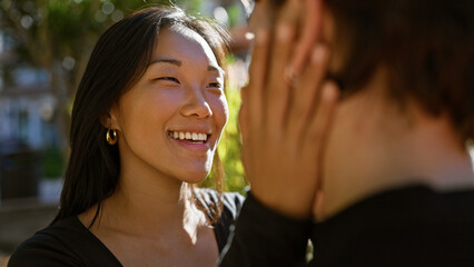 Close-up of a happy asian woman being affectionately touched by a man outdoors in sunlight
