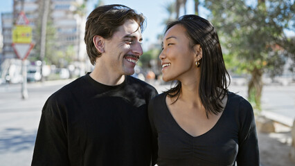 Obraz premium Interracial couple embracing happiness on a sunny urban street with woman and man smiling.