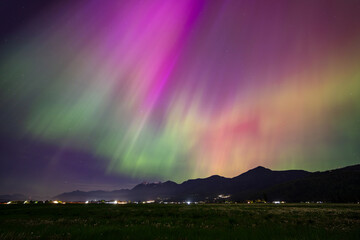 Radiant beams of green and purple light dance across the night sky above a Mountain Range