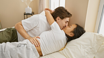 Interracial couple in love sharing an intimate moment in a cozy bedroom, with a woman and man embracing each other.