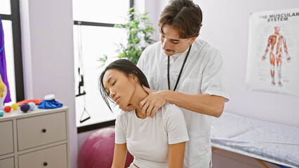 A male therapist performs a neck adjustment on a female patient in a brightly lit physical therapy...
