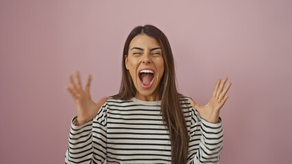 Hispanic woman screaming isolated against a pink wall background, portraying emotion and excitement.
