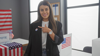 A young hispanic woman with an 'i voted' sticker points to herself in an american electoral college room with flags.