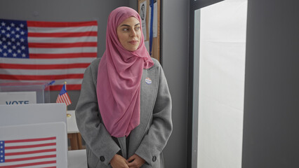 A young woman wearing a hijab stands with a proud expression in an american voting center,...