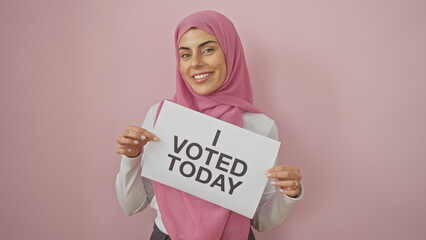 A cheerful woman holding a sign that says 'i voted today' against a pink background embodies...