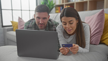 Couple shopping online together on a laptop in their cozy living room with the woman holding a...
