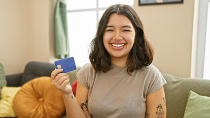 Smiling young hispanic woman holding credit card indoors.