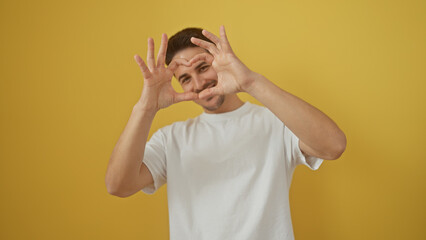 A cheerful man making heart shape with hands against a yellow background, evoking positivity and...