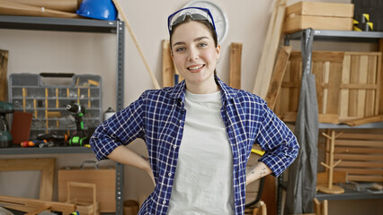 Confident young woman in a carpentry workshop posing with a smile, reflecting skilled woodworking...