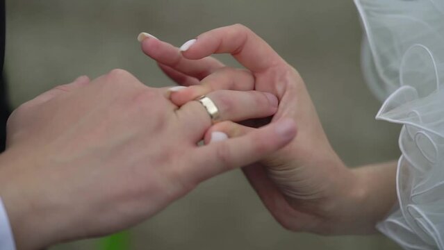 Bride and groom at wedding ceremony. Man put on a ring on a woman finger. Exchange jewelry rings, symbol of love. Outdoors in summer.