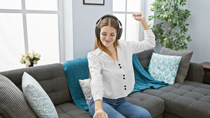 A cheerful young woman wearing headphones dances in a cozy living room, embodying relaxation and...