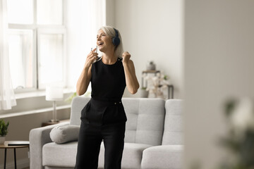 Positive excited mature singer woman in headphones singing at smartphone, recording voice, song, training vocal, listening to music from Internet playlist, having fun, enjoying creative activity
