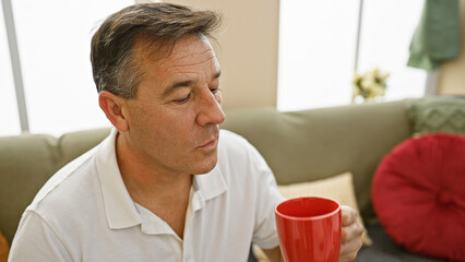 A pensive middle-aged man holding a mug in a cozy living room setting, exuding a sense of...