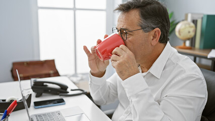 Mature businessman drinking coffee in a modern office setting, exuding a sense of professionalism...