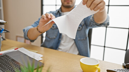 A bearded man tearing paper in an office, expressing frustration or termination of a document,