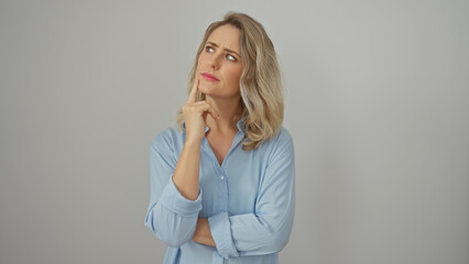 A thoughtful young blonde woman in a blue shirt poses against a white background, conveying a sense...