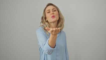 A young caucasian woman in a blue shirt blows a kiss against a white isolated background.
