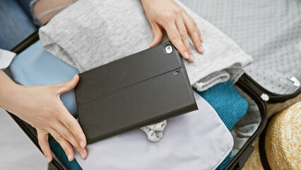 A woman packs clothing and a tablet into a suitcase, suggesting preparation for travel or a business trip.