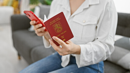 A woman holds a finnish passport and a smartphone in a modern living room, planning a trip.