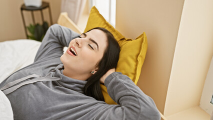 A relaxed young hispanic woman lies in bed with eyes closed and a joyful expression in a cozy...
