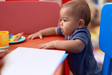 Adorable chinese toddler leaning on table standing at kindergarten