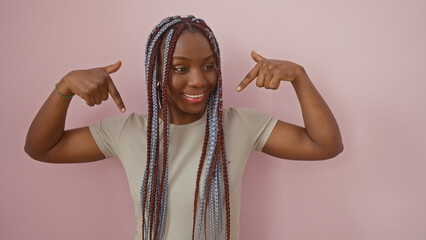 Smiling african american woman with braids pointing at herself against a pink isolated background