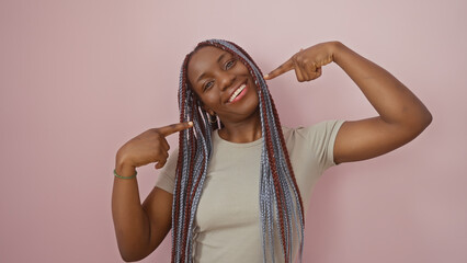 Beautiful african woman with braids pointing at her smile against a pink isolated background